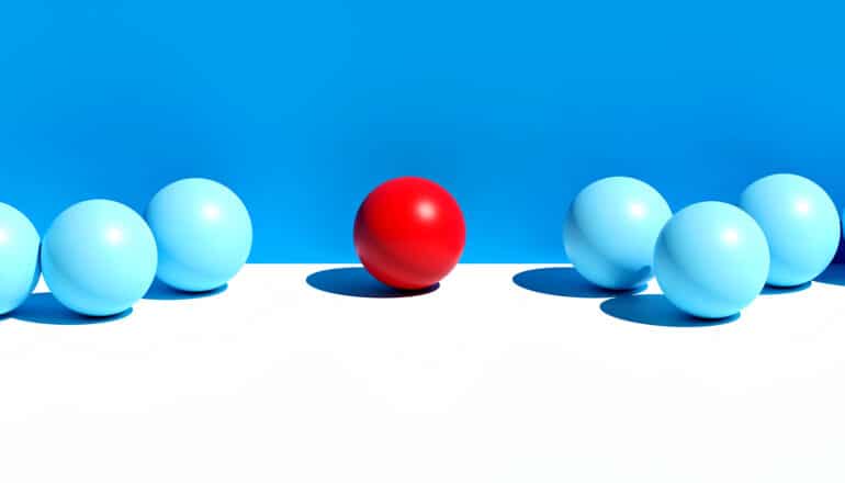 A single red ball stands apart from a row of blue balls sitting on a white surface.