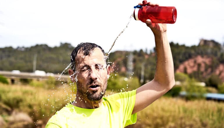 A man pours water on his head while standing outside in the heat.