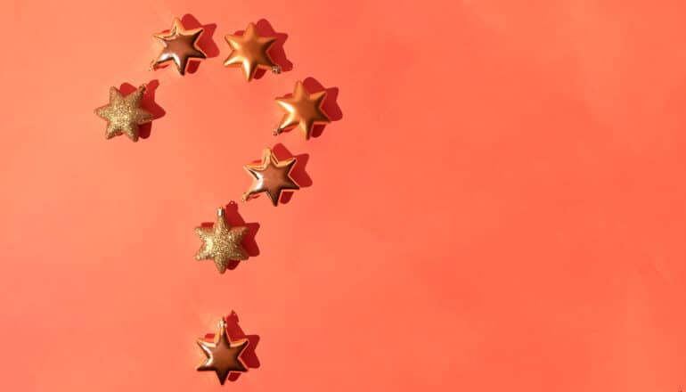 Golden star ornaments are arranged in the shape of a question mark on an orange surface.