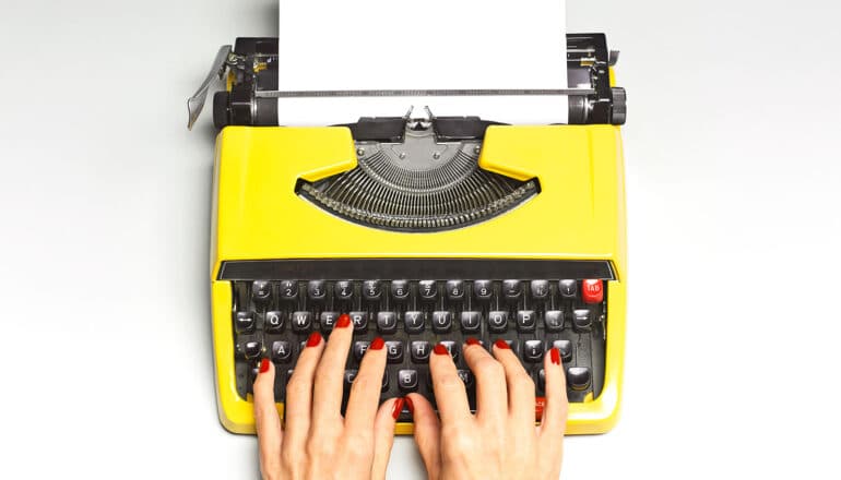 A person types on a yellow typewriter.