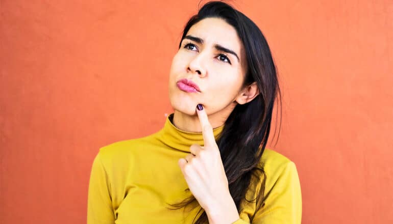 A young woman touches her chin with her index finger and looks lost in thought.