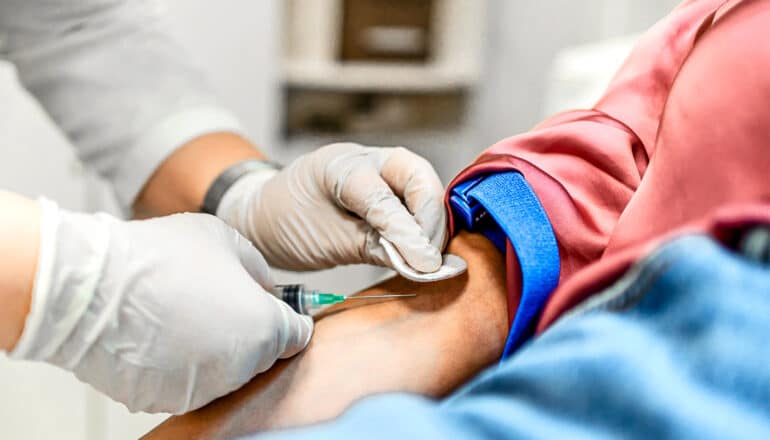 A doctor draws blood from a patient's arm while they are in a hospital.