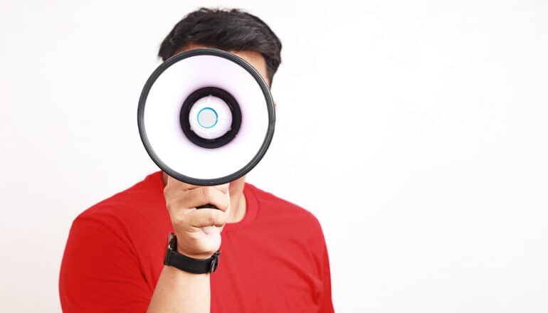 A man holds a megaphone that's covering his face.