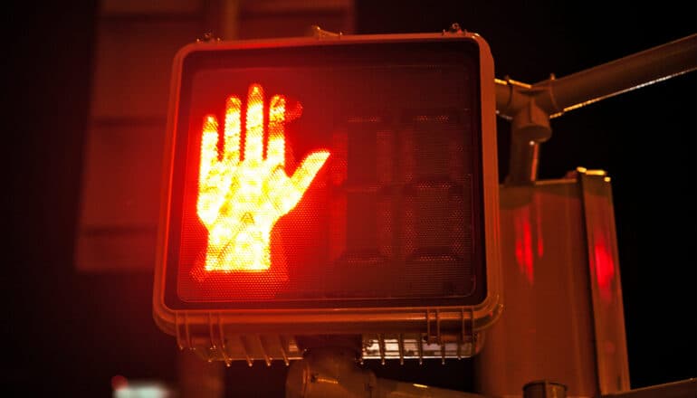 A crosswalk sign with a red hand indicating "stop."