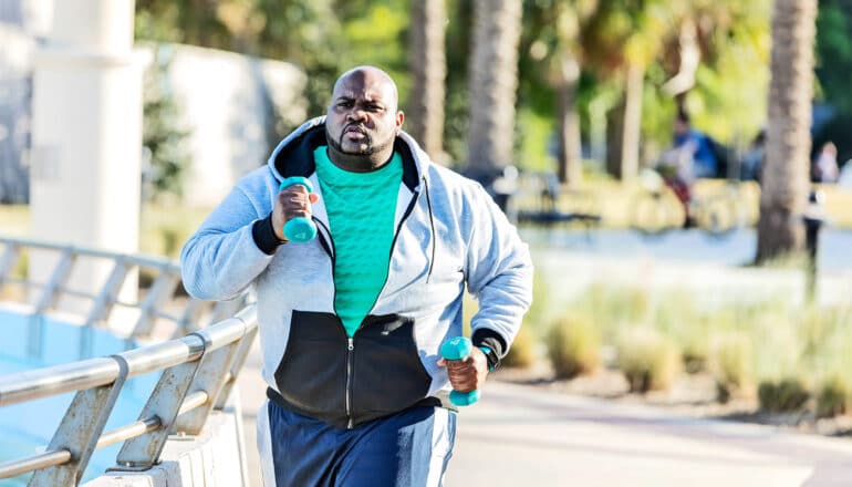 A man runs in a park while carrying small weights.