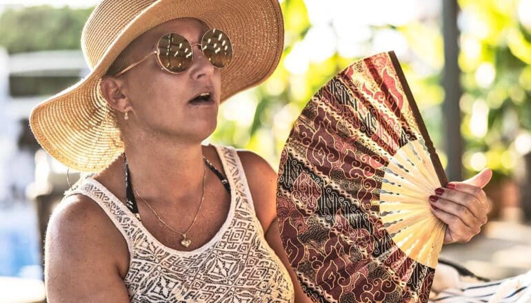 A woman in sunglasses and a wide-brimmed hat fans herself in the heat.