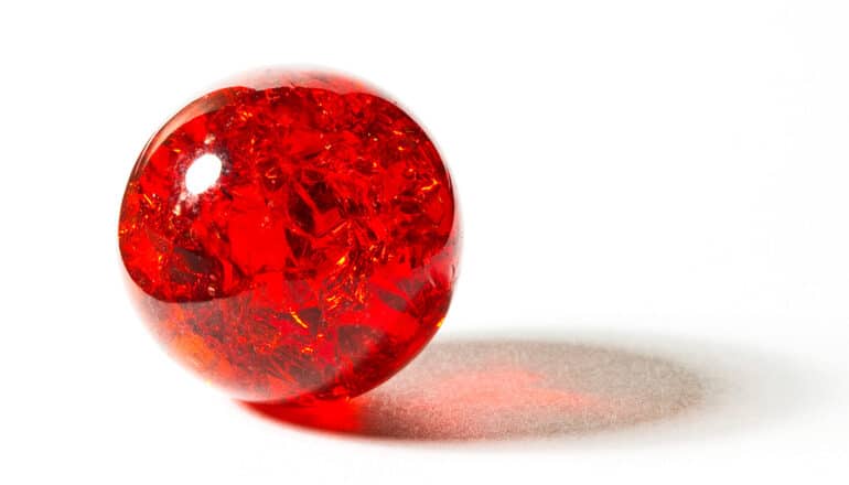 A red marble sits on a white surface with light shining through it.