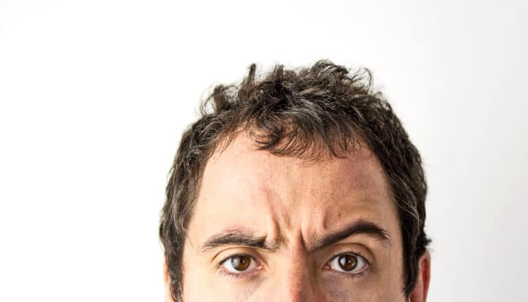 The top half of a man's face against a white background as he furrows his eyebrows.