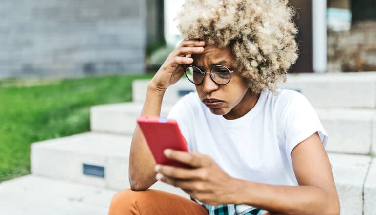 A woman looks at her phone with an exasperated look on her face.