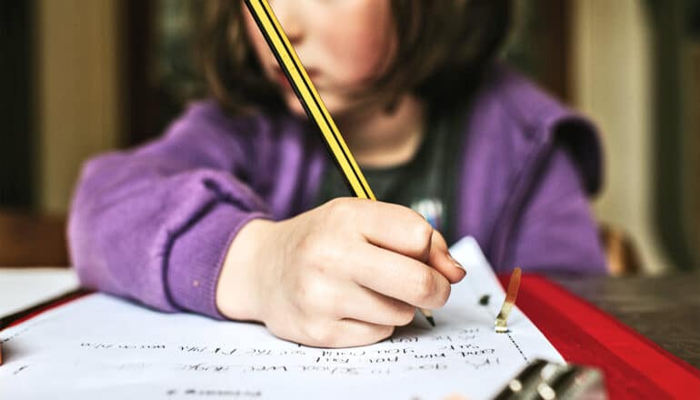 A young girl writes with a pencil in a binder.