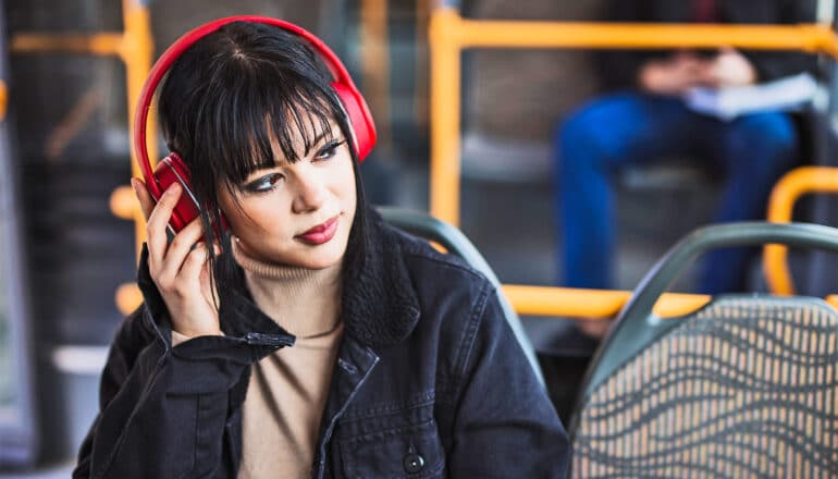 A young woman wearing red headphones while sitting on a bus and looking out the window.