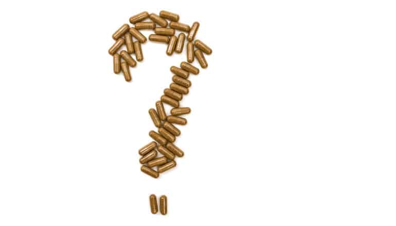 Many capsules filled with brown powder arranged in the form of a question mark on a white background.