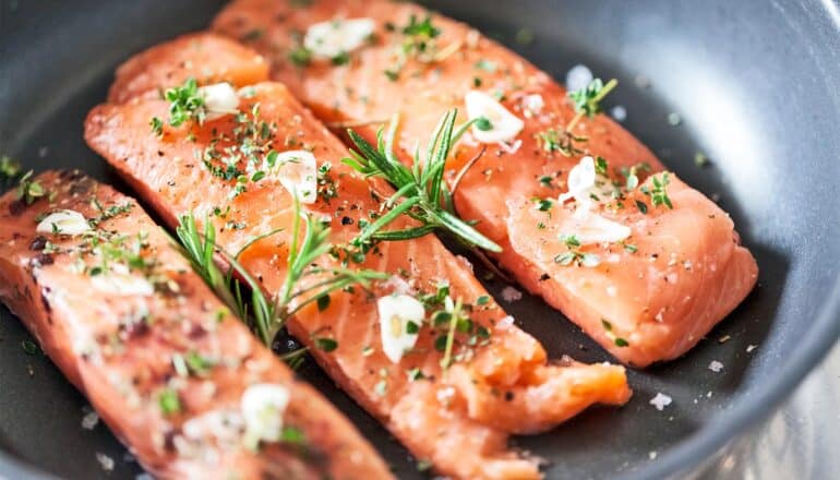 Three pieces of salmon cooking in a pan.