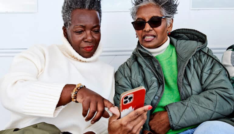 Two women look at a phone with skeptical faces.