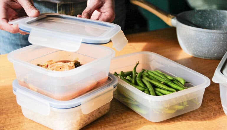 A person puts leftover food into plastic containers.