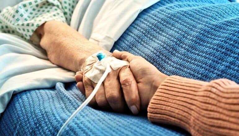 A hospital patient in bed holds hands with a relative.