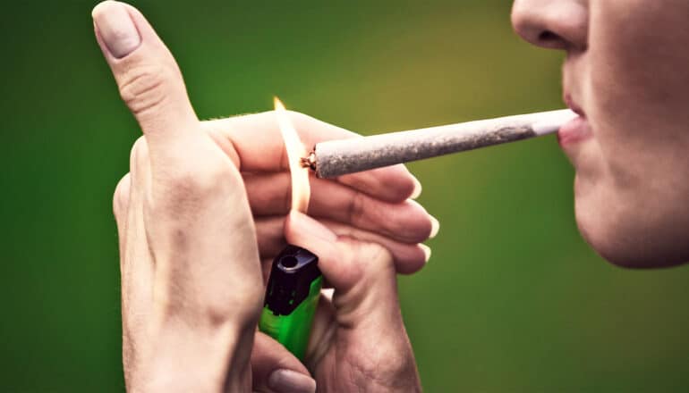 A young woman lights a marijuana joint.