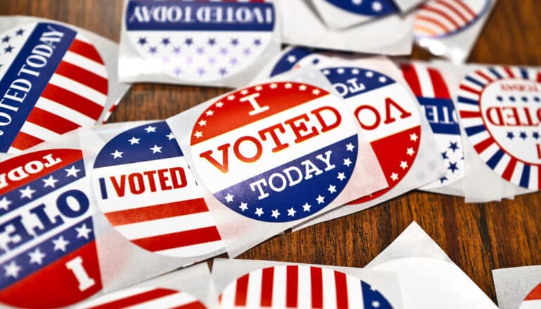 Many "I voted" stickers sit in a pile on a folding table.