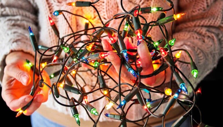 A person tries to untangle colorful holiday lights.