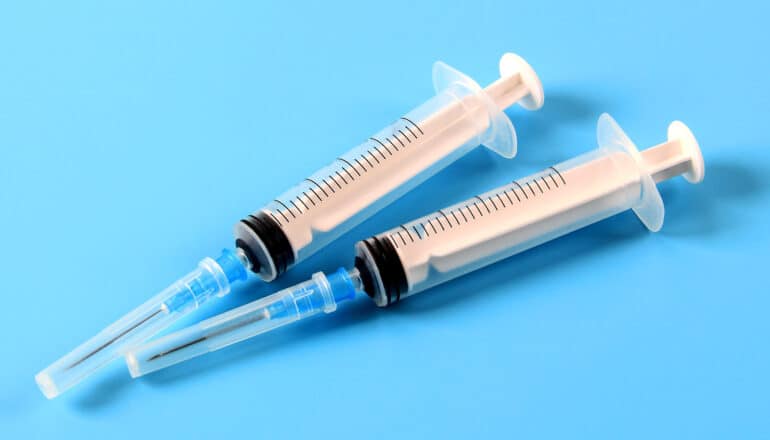 Two syringes lay on a light blue background.