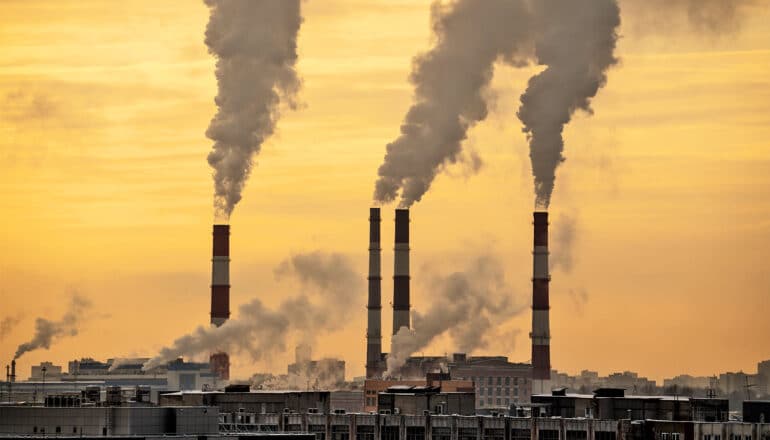 A power plant emits brown clouds of smoke via smokestacks at sunset.