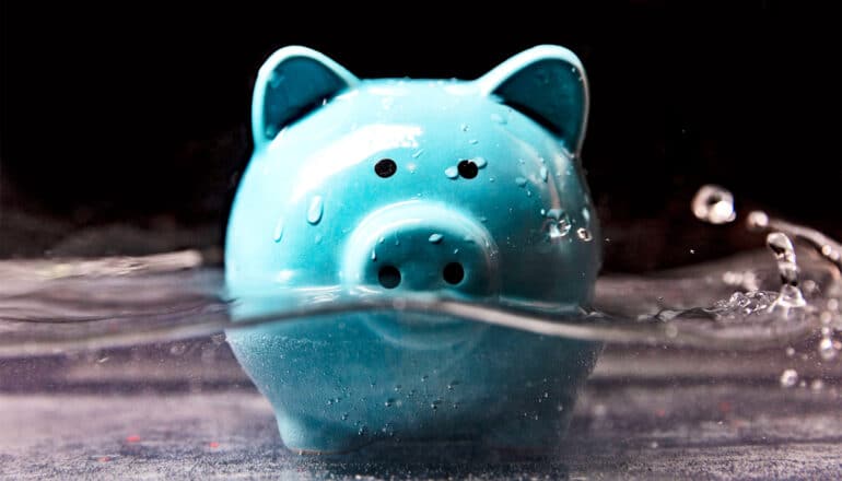 A blue piggy bank is half-submerged in water against a black background.