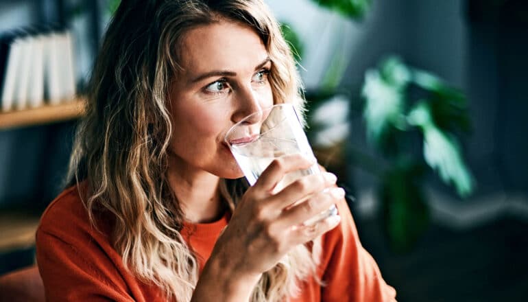 A woman drinks a glass of ice water while sitting in an office.