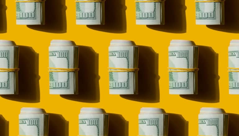 Several rolls of 100 dollar bills in rows on a yellow background.