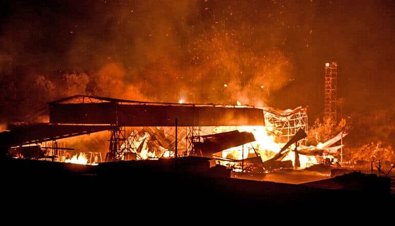 A building burns at night as smoke and embers rise into the air.