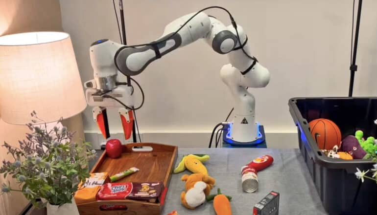 A robot arm places an apple on a tray as it separates toys and food on a cluttered table.