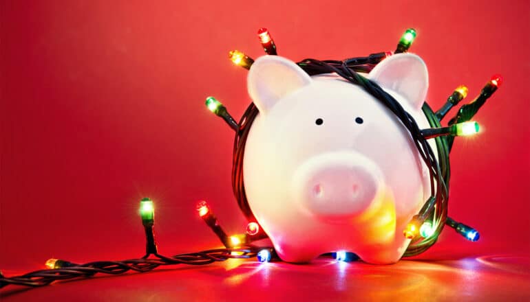 Colorful Christmas lights wrapped around a white piggy bank on a red background.