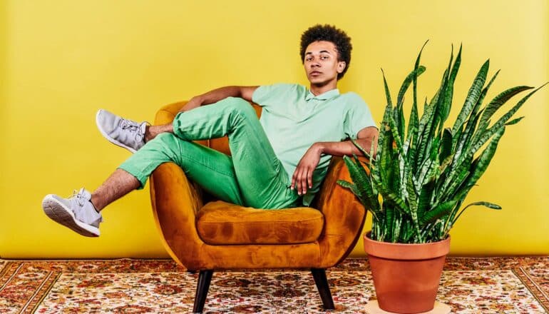 A young man sits in a chair with his legs over its arm.