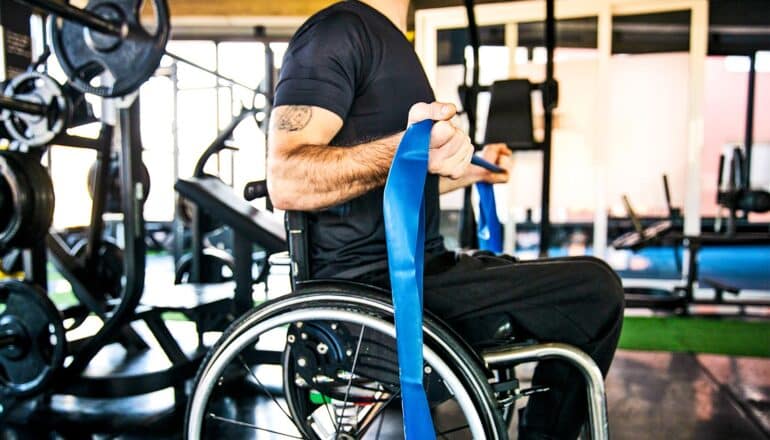 A man in a wheelchair uses a blue band to exercise his arms.