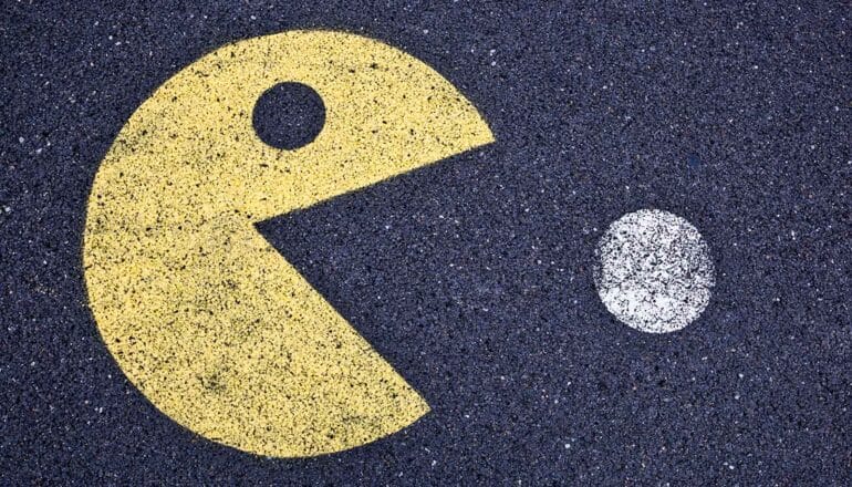 An image of the video game character Pac-Man eating a white dot painted on asphalt.