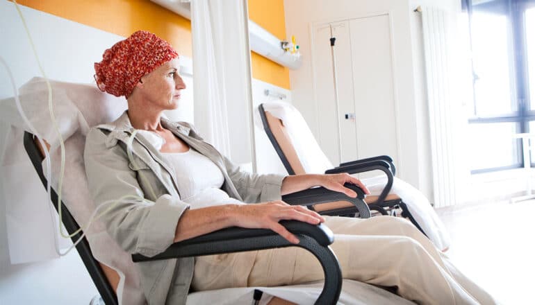 A woman wearing a wrap on her head sits while hooked up to a chemotherapy IV.