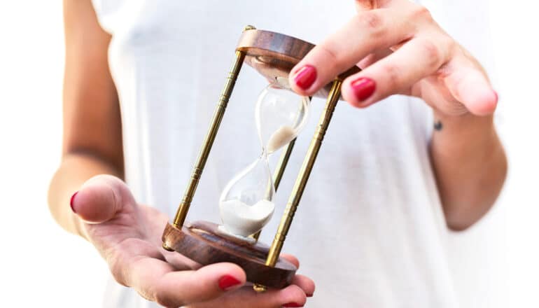 A woman turns an hourglass filled with sand over in her hands.