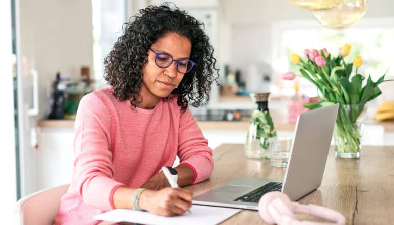 A woman writes on paper while working at her kitchen table.