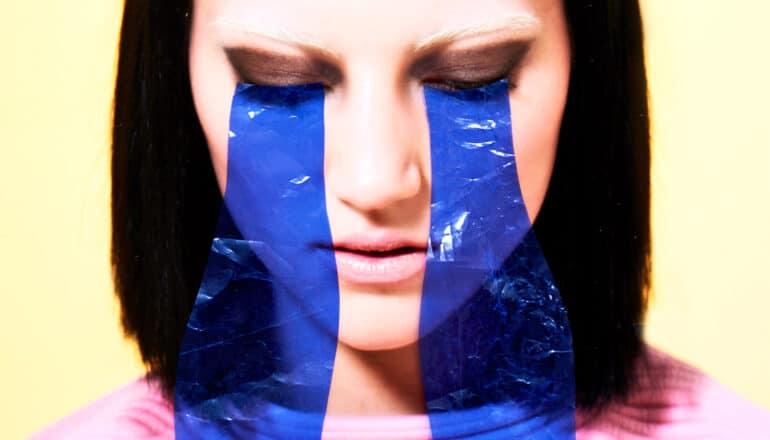 A young woman looks down and has blue cellophane collaged over her face to look like tears.