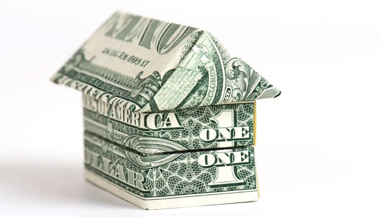 Dollar bills folded to look like a small house on a white background.