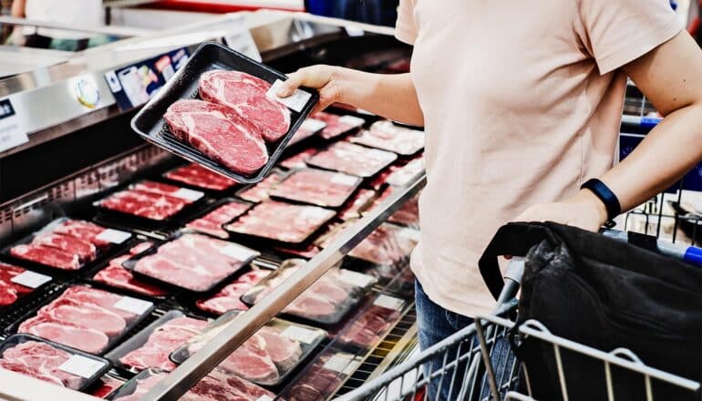 A woman picks meat up from a butcher's display in the supermarket.