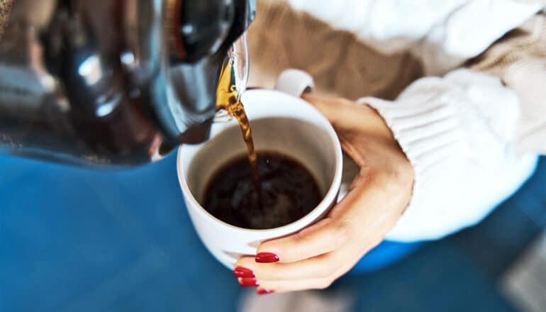 A woman pours herself a cup of coffee from a large pot.