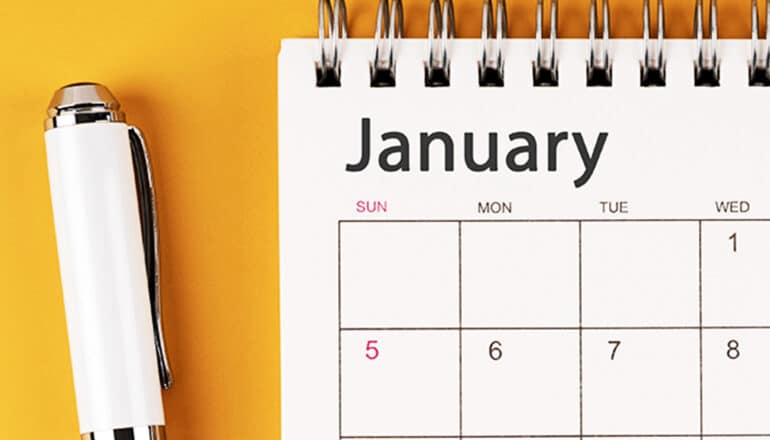 A calendar opened to the January page sits on a yellow surface next to a white pen.