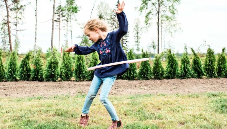 A young girl strikes a pose while hula hooping in a backyard.