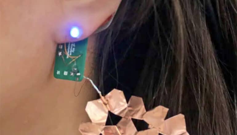 A person wears an earring with a glowing LED light powered by the new technology.