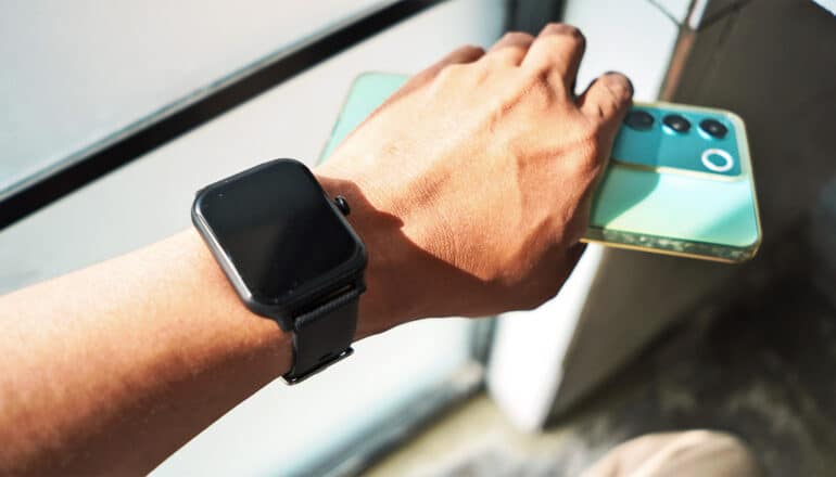 A man holds his phone in the same hand that has a smartwatch on the wrist.