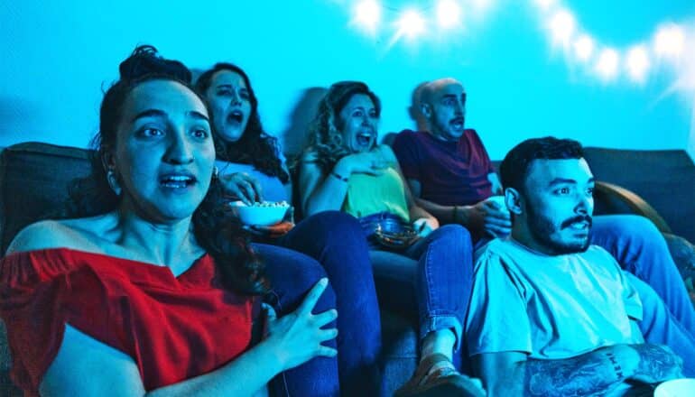 A group of people watch a movie with varying reactions from suspense to shock.