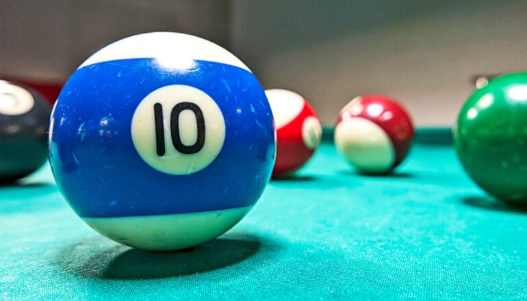 A pool ball with the number ten on it sits on a green pool table with other balls behind it.