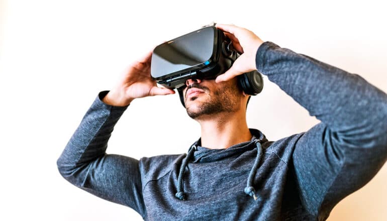 A young man puts a virtual reality headset over his eyes.