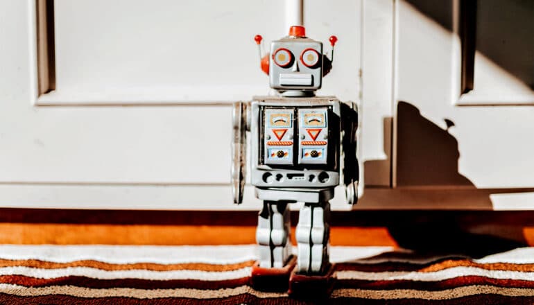 A toy robot stands near a door casting a shadow on the wall behind it.