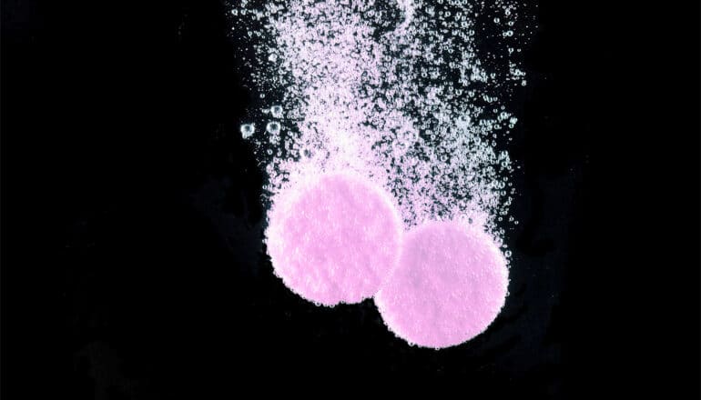 Two pink pills dissolve in water against a black background.